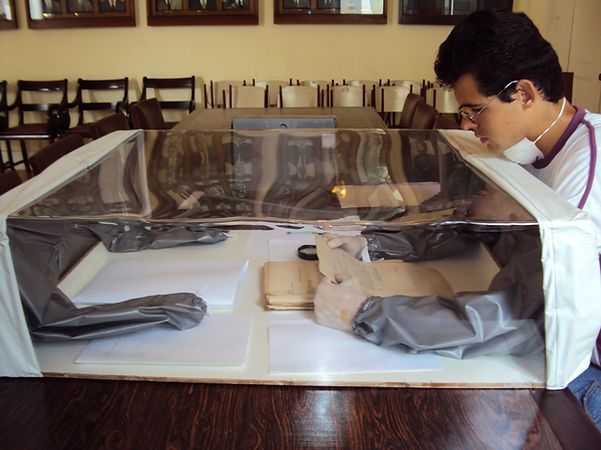 Pesquisador fazendo uso da capela de higienização para consultar documento antigo.
